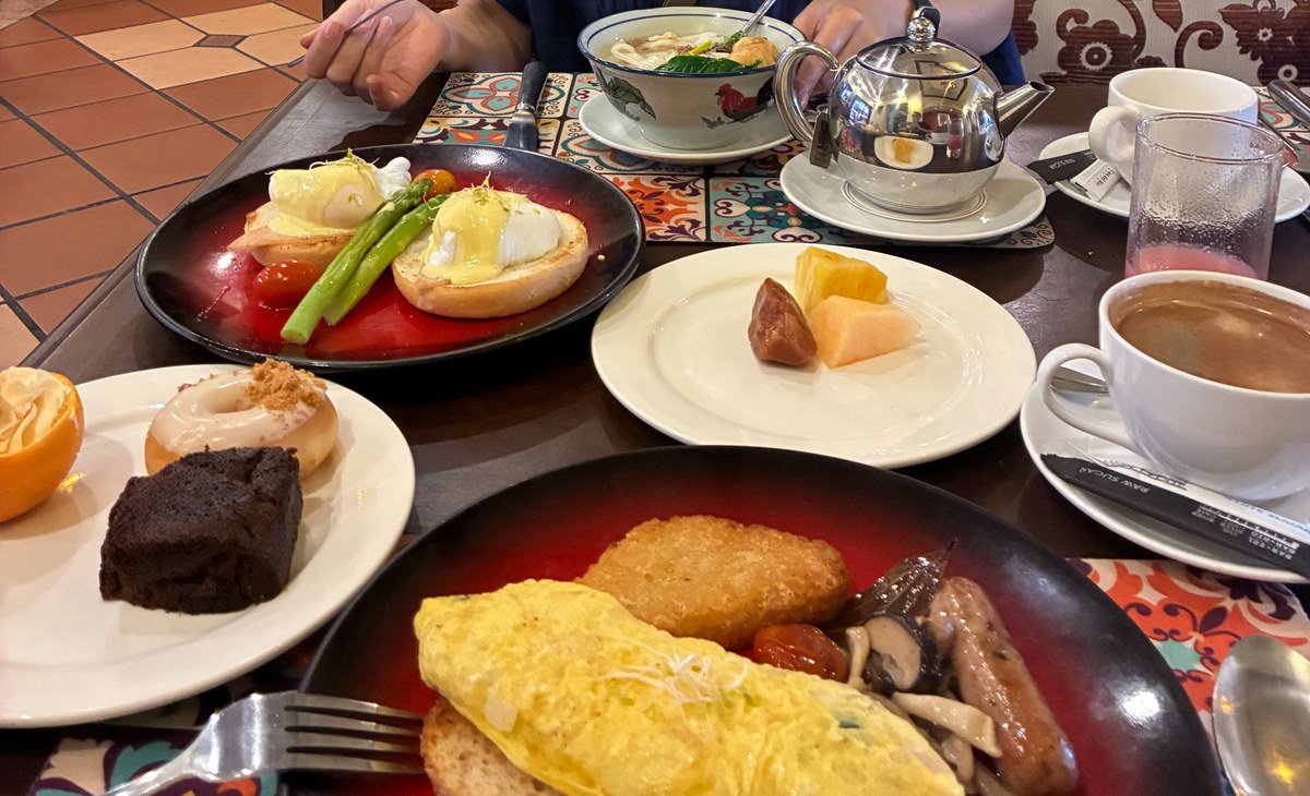 テーブルいっぱいに並んだ朝食。米粉の麺、エッグベネディクト、オムレツ、フルーツ、コーヒー